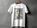 Against a gray background, a white tee by Garment Graphics hangs on a wooden hanger. Ideal for casual outings, it displays a cartoon alligator with a basketball and the phrase SEE YOU LATER ALLIGATOR, encapsulating playful style effortlessly.