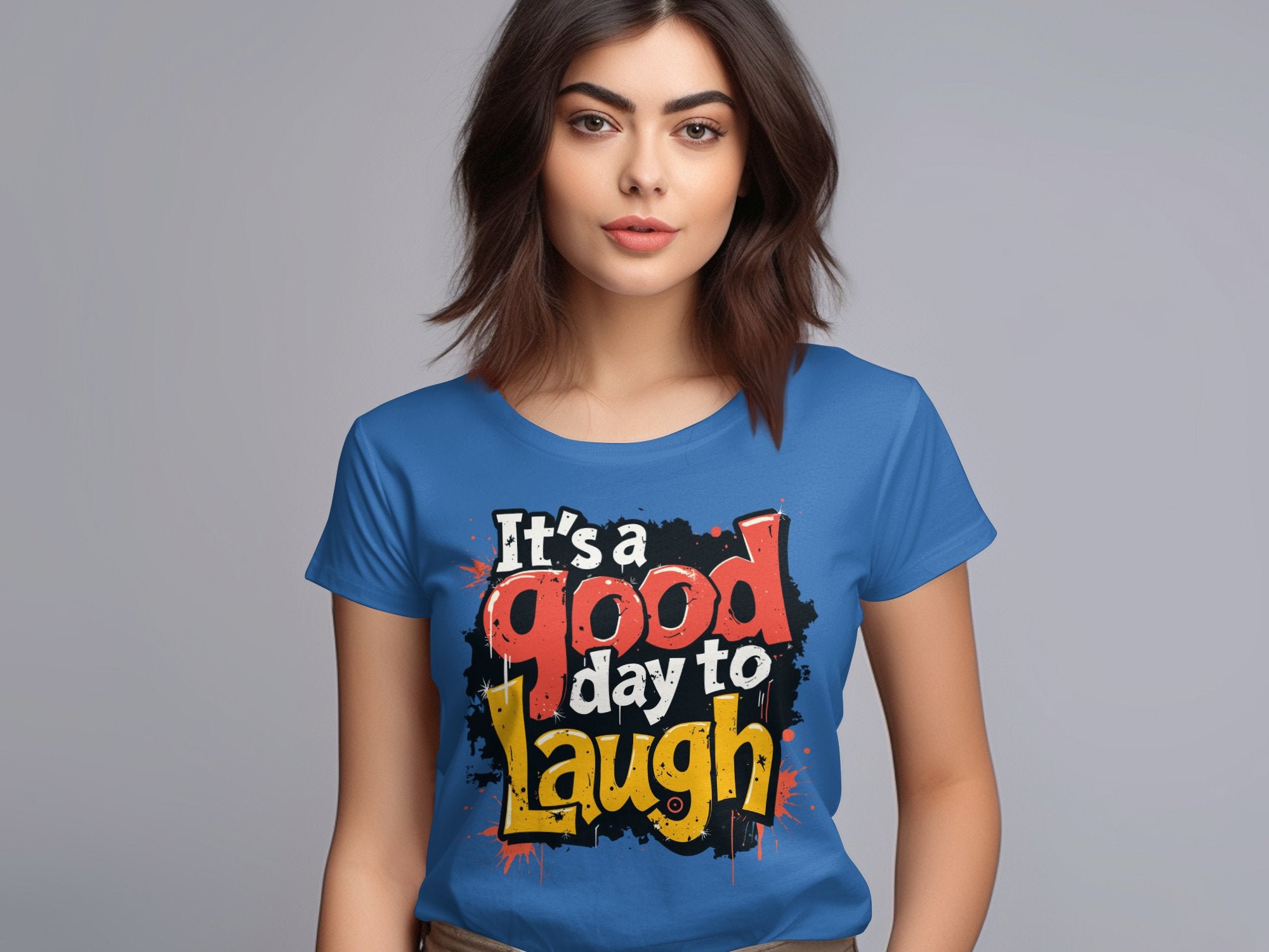 A woman stands against a neutral background, radiating positivity in a semi-fitted blue T-shirt from Garment Graphics, featuring the colorful text Its a good day to laugh.