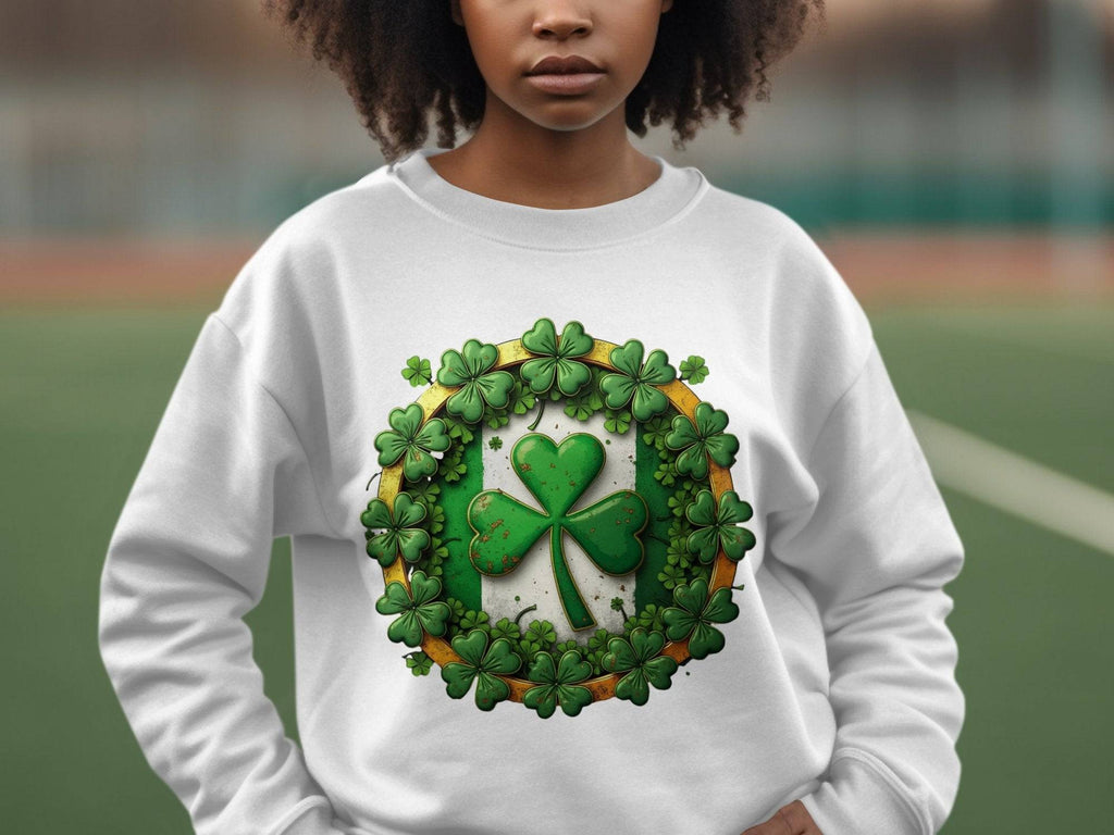 A person wears a Garment Graphics white sweatshirt featuring a large green shamrock, embodying the Irish spirit, surrounded by smaller shamrocks in a circle. The blurred outdoor field enhances the charm of this Circle Design Sweatshirt.