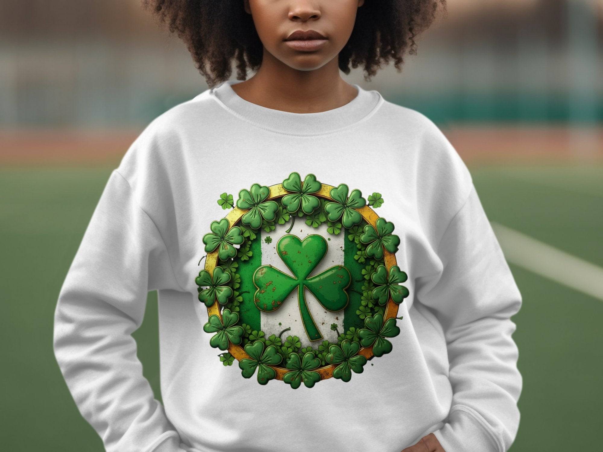 A person wears a Garment Graphics white sweatshirt featuring a large green shamrock, embodying the Irish spirit, surrounded by smaller shamrocks in a circle. The blurred outdoor field enhances the charm of this Circle Design Sweatshirt.