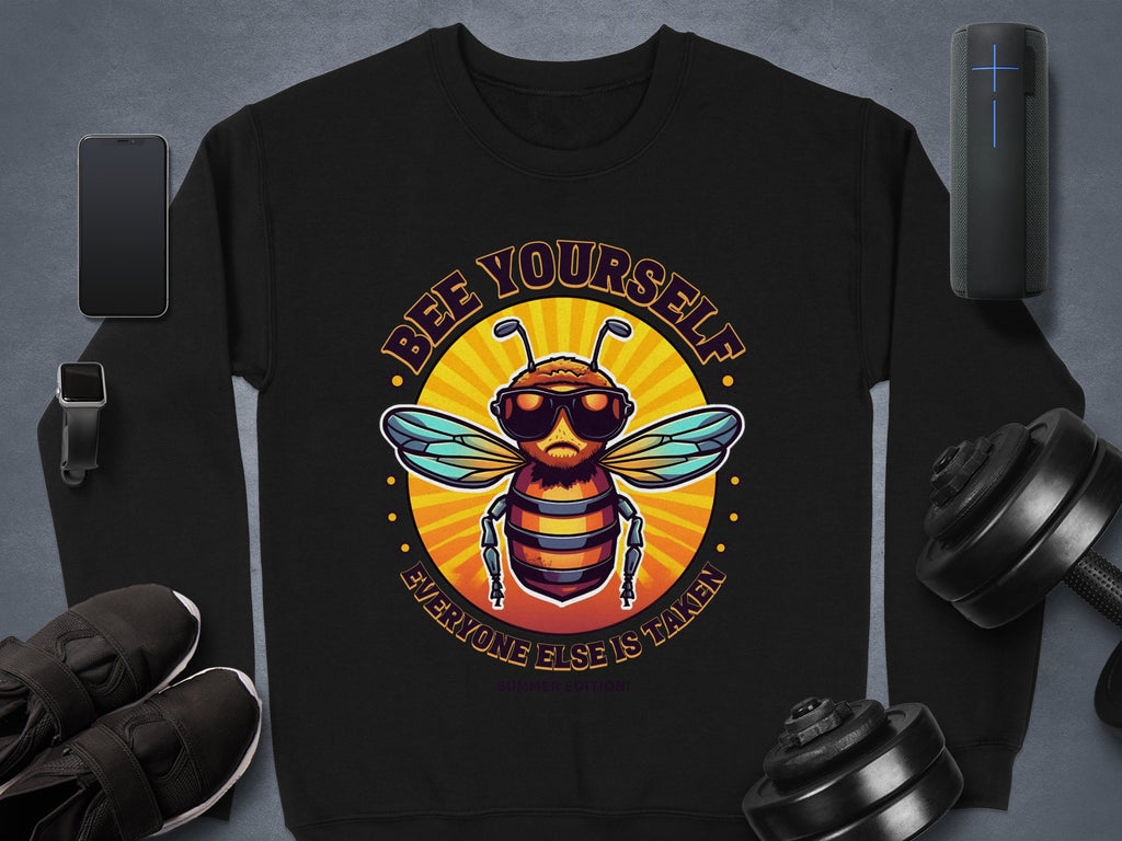 Garment Graphics black unisex sweatshirt, from the Summer Edition, showcases a vibrant bee in sunglasses with the text Bee Yourself Everyone Else Is Taken, set amidst gadgets and gear on a gray background.
