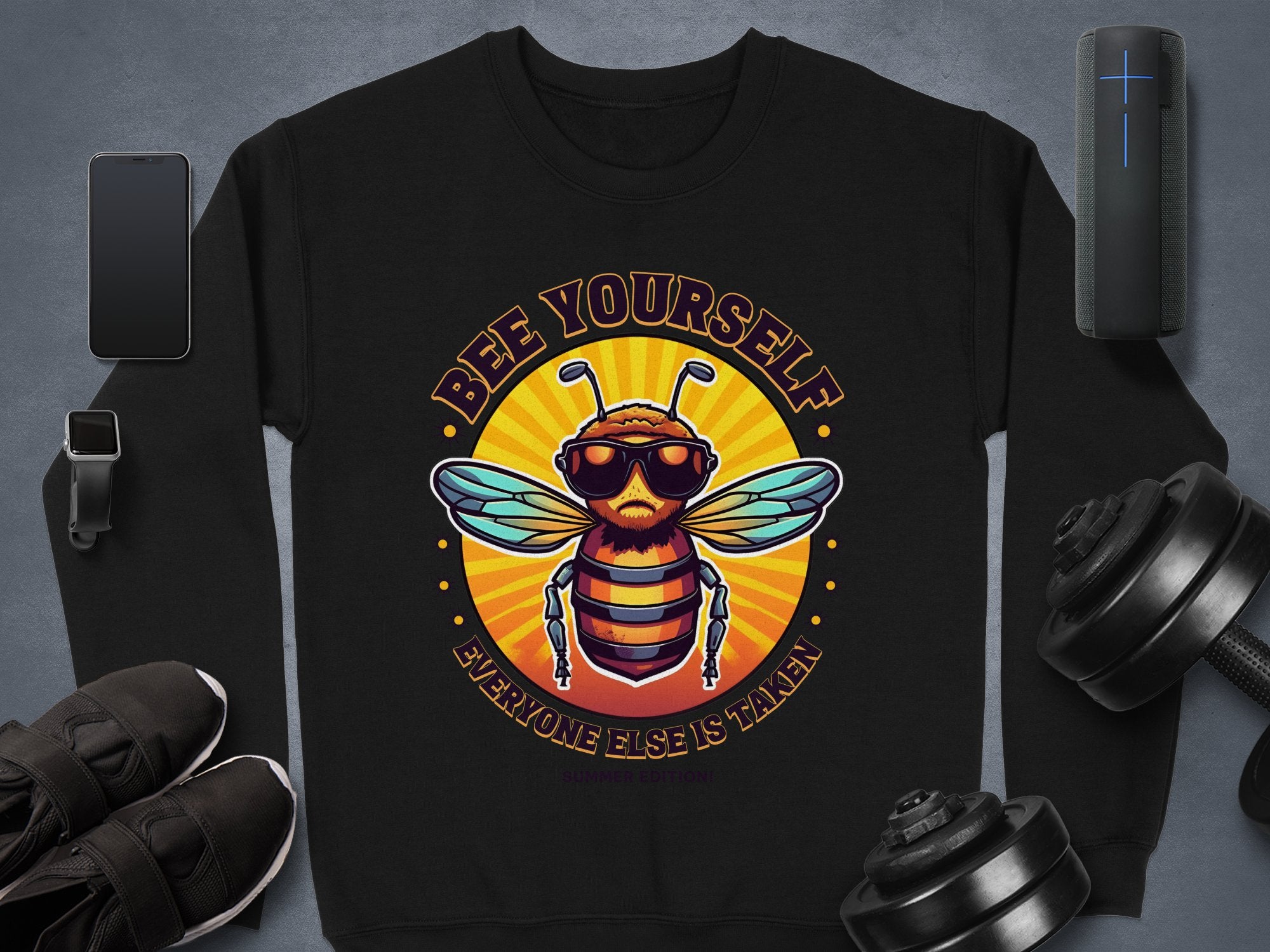 Garment Graphics black unisex sweatshirt, from the Summer Edition, showcases a vibrant bee in sunglasses with the text Bee Yourself Everyone Else Is Taken, set amidst gadgets and gear on a gray background.