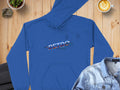 A blue Garment Graphics hoodie featuring the vibrant RETRO design is displayed on a wooden surface, accompanied by a denim jacket for a trendy modern look. Nearby are a latte with artistic foam, a potted plant, and a rock.