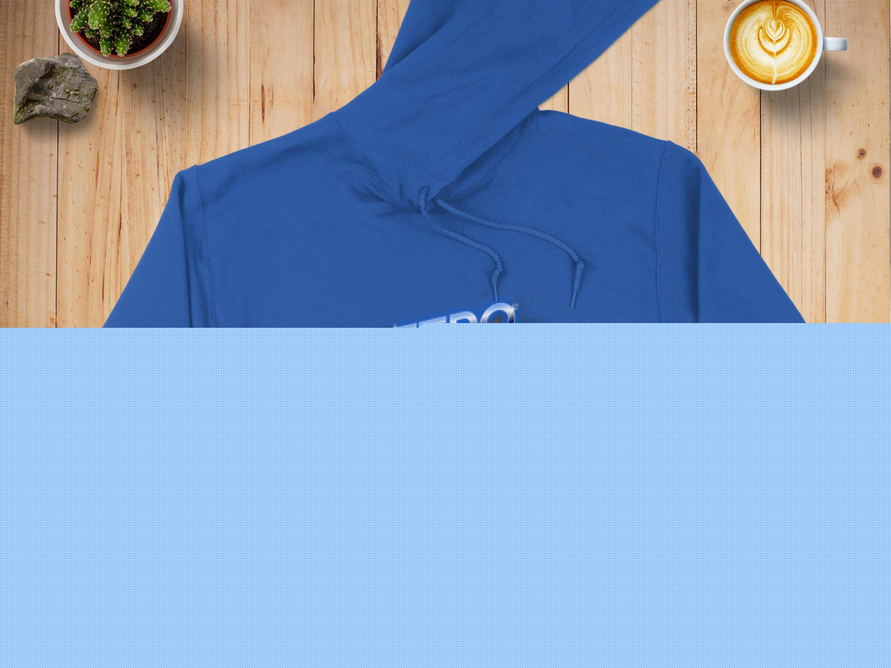 A blue Garment Graphics hoodie featuring the vibrant RETRO design is displayed on a wooden surface, accompanied by a denim jacket for a trendy modern look. Nearby are a latte with artistic foam, a potted plant, and a rock.