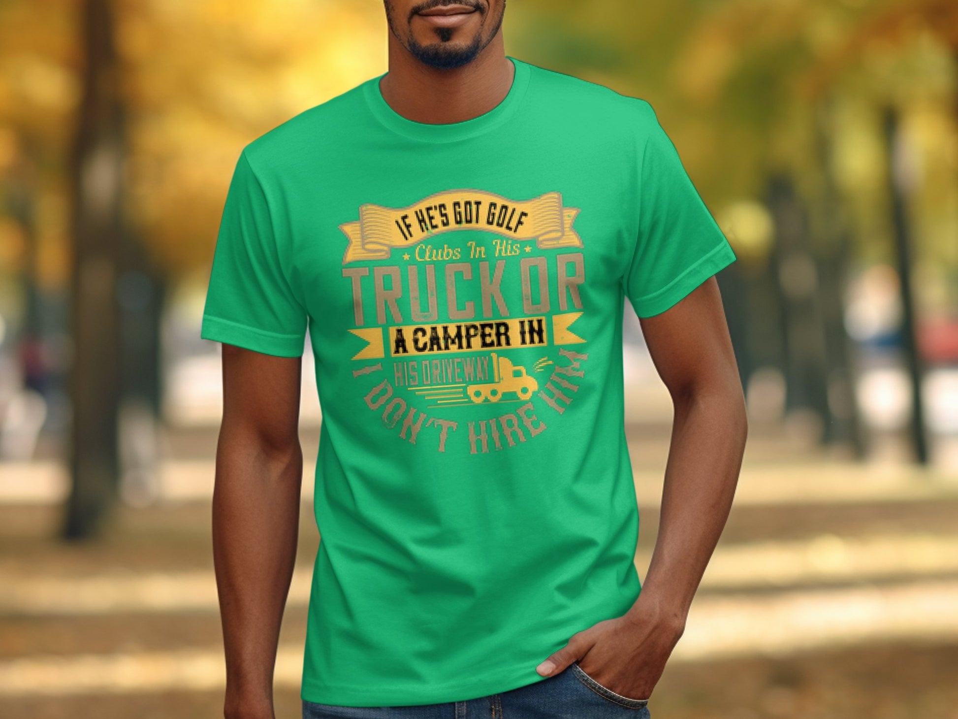 A person outdoors sports a green Garment Graphics T-shirt with the slogan: If hes got golf clubs in his truck or a camper in his driveway, I dont hire him, set against a backdrop of autumn trees lining a pathway, highlighting camping humor.
