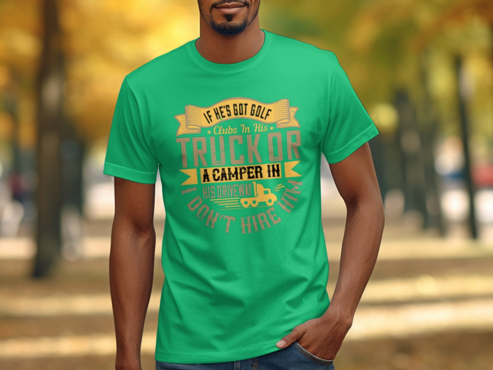 A person outdoors sports a green Garment Graphics T-shirt with the slogan: If hes got golf clubs in his truck or a camper in his driveway, I dont hire him, set against a backdrop of autumn trees lining a pathway, highlighting camping humor.