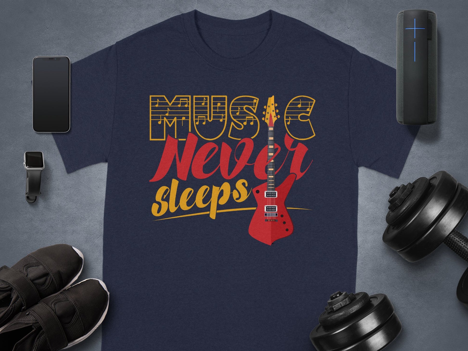 A navy blue graphic t-shirt by Garment Graphics, made of 100% cotton, features Music Never Sleeps with a red guitar. Pair it with a smartphone, smartwatch, wireless speaker, black sneakers, and an adjustable dumbbell for the perfect look.