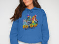 A woman confidently poses against a plain backdrop wearing a blue Garment Graphics hoodie, featuring vibrant dancer images and Risk Taker Street Dance 10th Final. Her hands rest casually in her pockets, exuding an effortlessly stylish vibe.