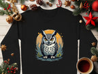 This black, long-sleeved unisex sweatshirt by Garment Graphics features a captivating owl design with piercing eyes, surrounded by Christmas decorations including ornaments, pine cones, stars, and a cozy coffee cup.