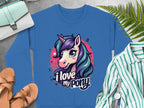 A blue Garment Graphics sweatshirt features a cartoon unicorn with a purple and teal mane, pink horn, and I love my pony text. Its on concrete with sandals, a striped shirt, watch, small bag, and ferns—ideal for unicorn enthusiasts.