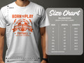 A man wears a white Garment Graphics T-shirt with bright orange text and a soccer design, featuring Born to Play, One Goal, One Dream, Young Squad Football. A Gildan 5000 heavy cotton football T-shirt size chart with inch measurements is nearby.