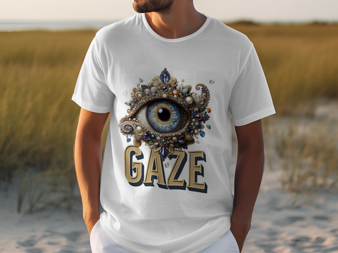 In a grassy, sandy landscape, a person wears a Garment Graphics classic fit white graphic T-shirt featuring an ornate eye design with GAZE boldly displayed.