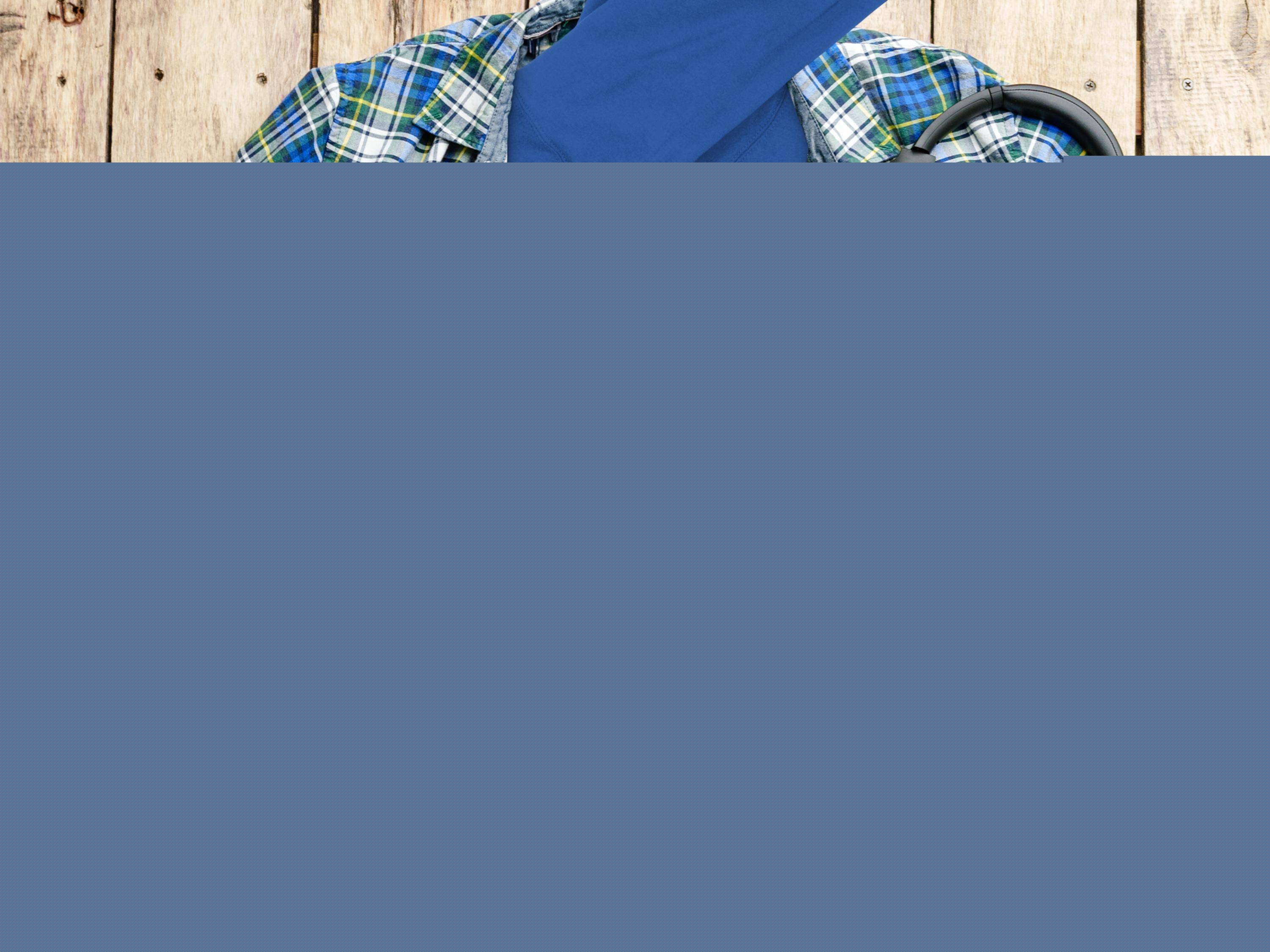 A blue Garment Graphics Turkey on the Run hoodie with a cartoon turkey graphic sits on a wooden surface. Nearby are a blue and green plaid shirt, camera, headphones, and lidded cup—ideal for fans of funny hoodies and photography.