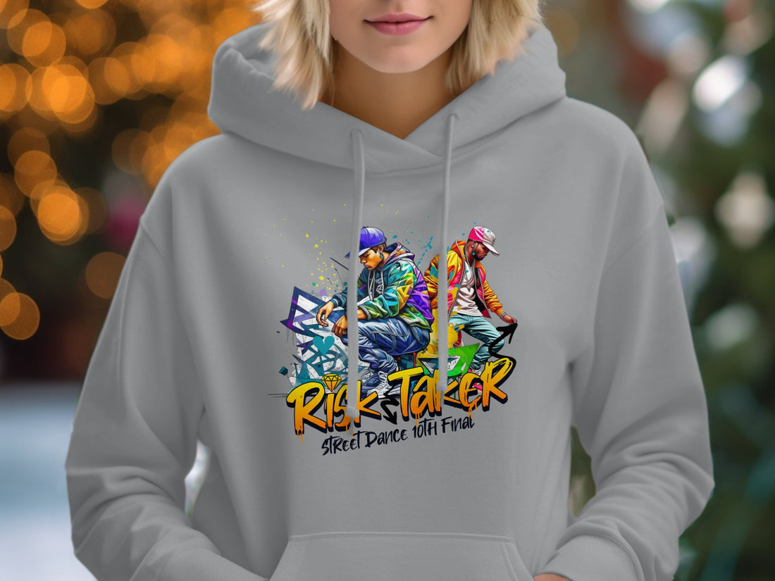 Garment Graphics presents a white hoodie featuring colorful dancer graphics and the phrase Risk Taker Street Dance. Accessories around it include a straw hat, sunglasses, camera, sandals, and notebook on a wooden surface.