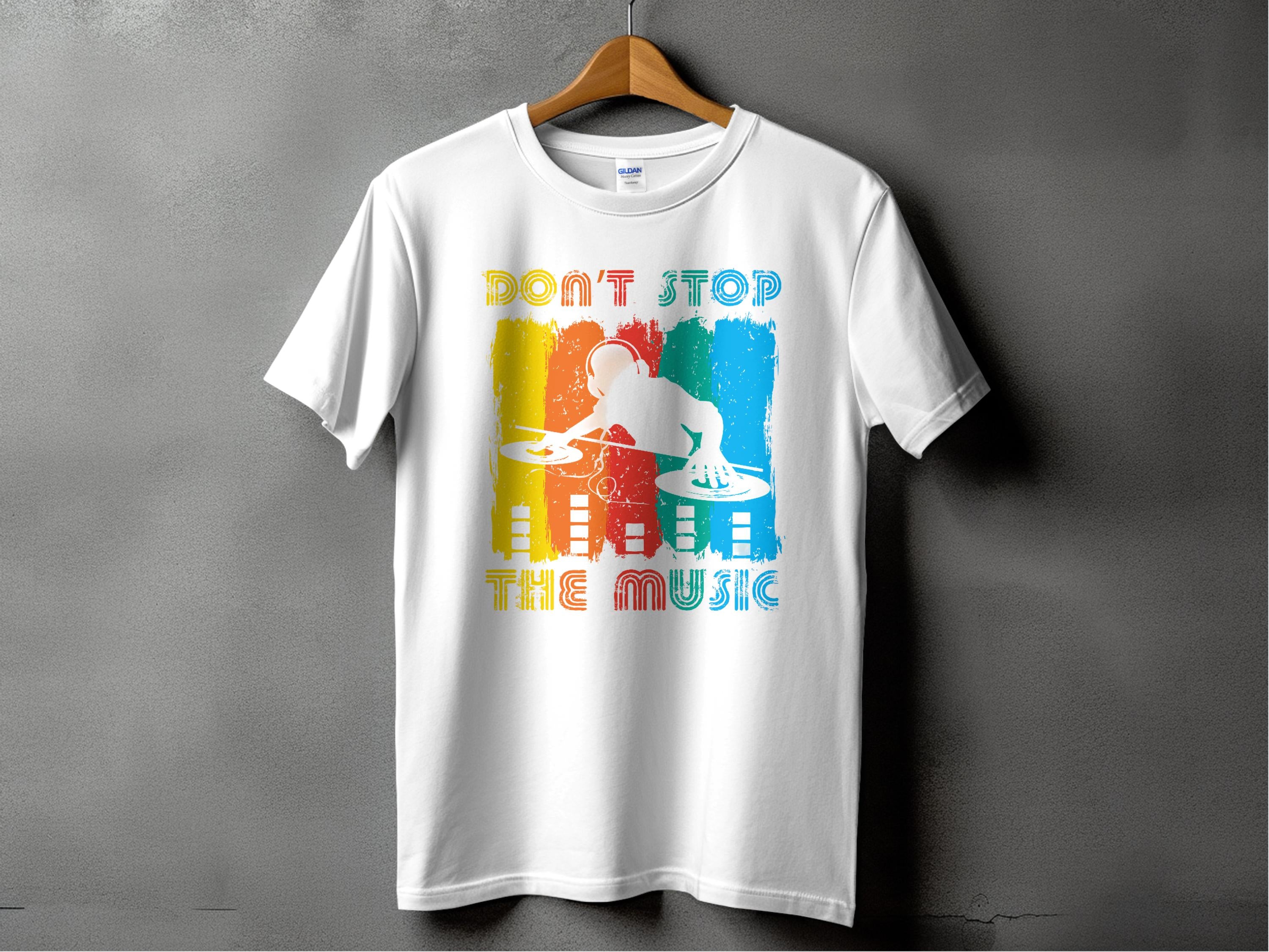 The Garment Graphics white T-shirt, displayed on a wooden hanger against a gray wall, features a vibrant DJ graphic at turntables with the bold motto Dont Stop the Music, making it perfect for music lovers and party-goers eager to dance.