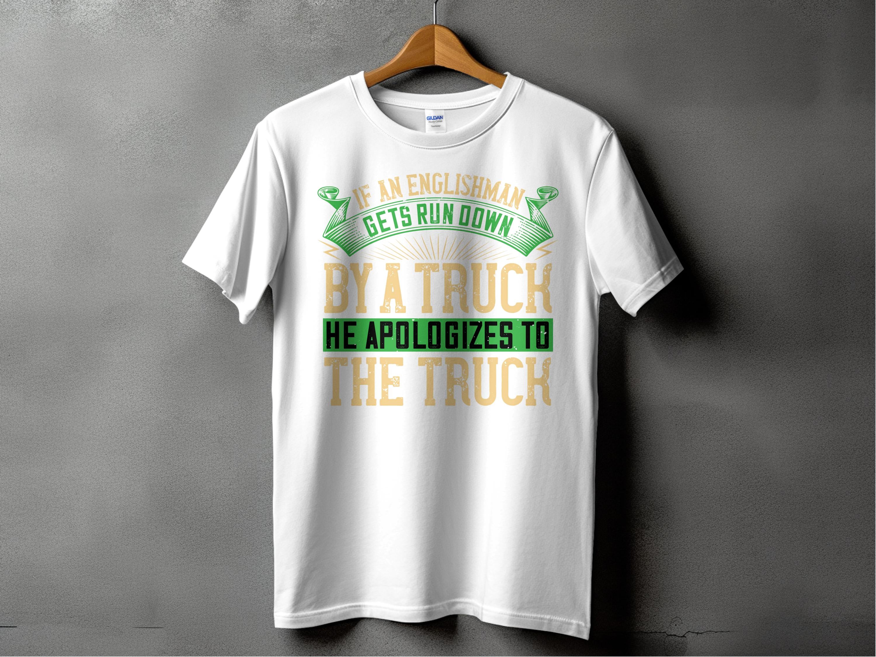 Garment Graphics white T-shirt showcases a clever design with the funny phrase If an Englishman gets run down by a truck, he apologizes to the truck, in green and gold, contrasting attractively against a textured dark gray background.