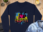 The Garment Graphics navy blue sweatshirt features an artistic graffiti design with I Love Graffiti in bold yellow letters, a red heart, and blue splashes. Styled on a wooden surface, its the perfect match with a denim jacket, latte, and small plant for an urban vibe.