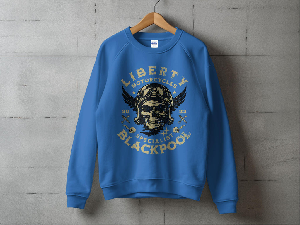 Garment Graphics blue sweatshirt on a wooden hanger against a concrete wall features a biker vibe with a skull in sunglasses, wings, and helmet, surrounded by Liberty Motorcycles Specialist Blackpool 2023 in distressed text.