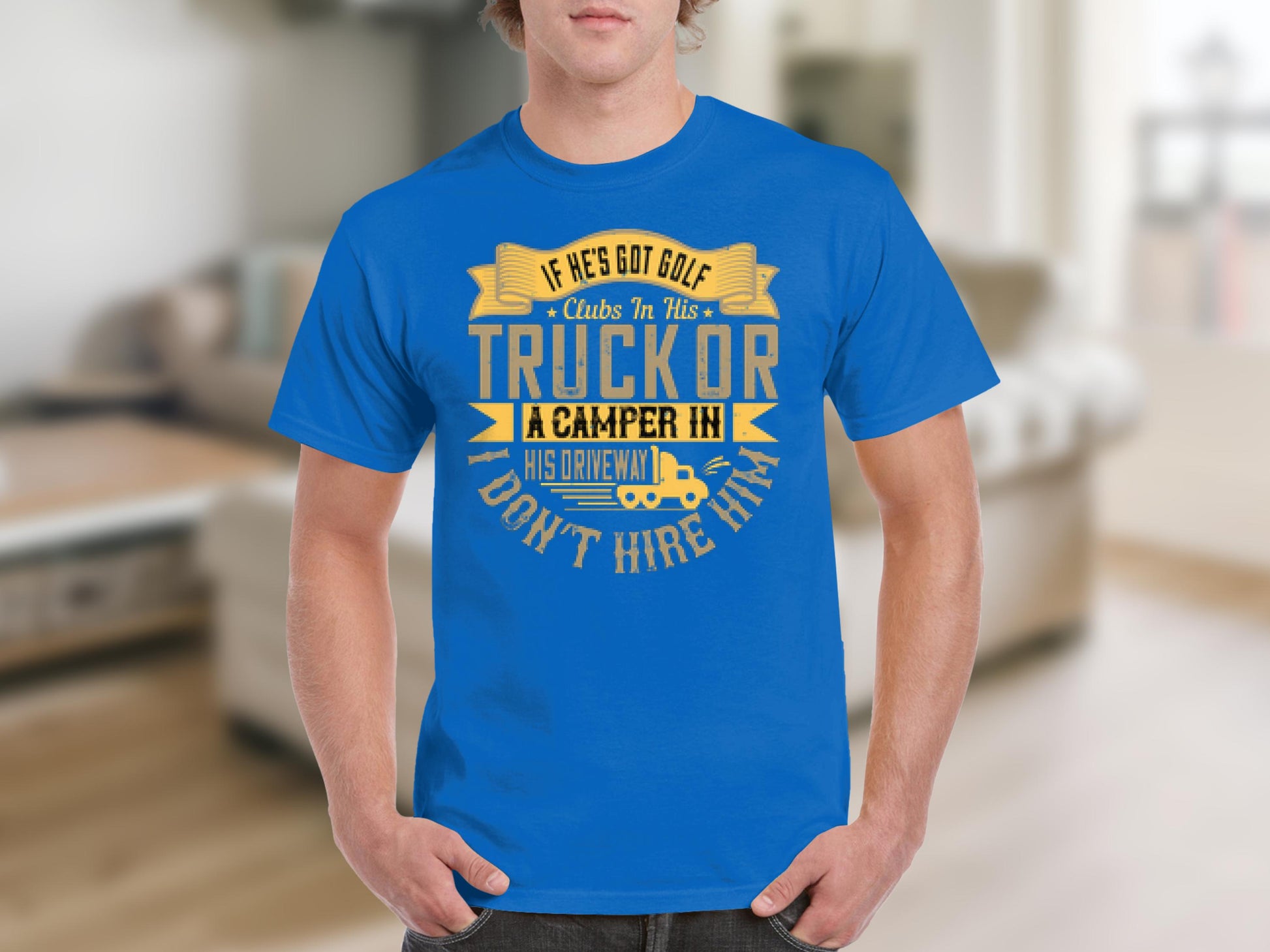 Someone wearing a blue T-shirt from Garment Graphics featuring the text: If hes got golf clubs in his truck or a camper in his driveway, dont hire him. The shirts camping humor stands out against what looks like a cozy, blurred living room background.