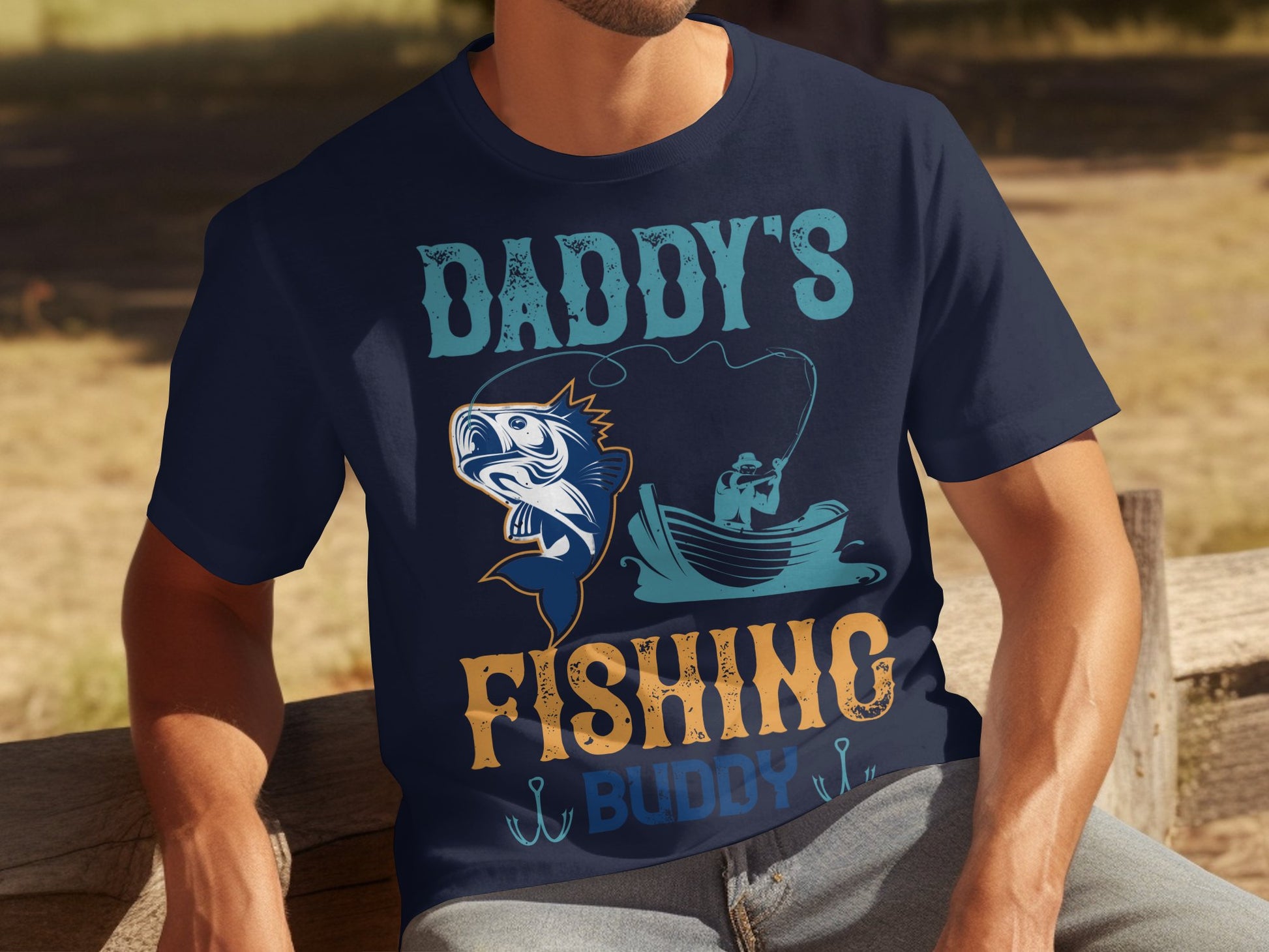 A fishing enthusiast unwinds on a wooden bench, wearing a navy graphic tee by Garment Graphics. The shirt displays Daddys Fishing Buddy with a colorful fish and someone casting from a boat illustration.