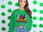 A woman stands against a shamrock-themed backdrop, wearing a Garment Graphics sweatshirt featuring a lively I Love Graffiti design. Her urban look is highlighted by long brown hair and denim shorts.
