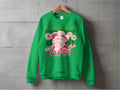 The Garment Graphics Wild Side Sweatshirt, in green and unisex sizing, hangs on a wooden hanger against a gray wall. It features bold graphics of a hatted figure with flowers and the phrase HANDS OFF! enhanced by pink and white flowers and hearts for an enchanting touch.