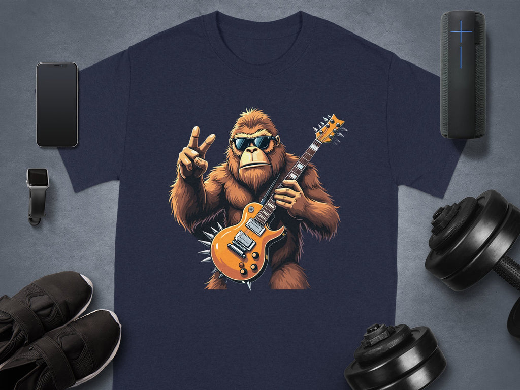 A navy T-shirt from Garment Graphics features a gorilla in sunglasses, jamming on an electric guitar, and flashing a peace sign. Ideal for music lovers, its surrounded by a smartphone, smartwatch, Bluetooth speaker, shoes, and dumbbells on a gray surface.