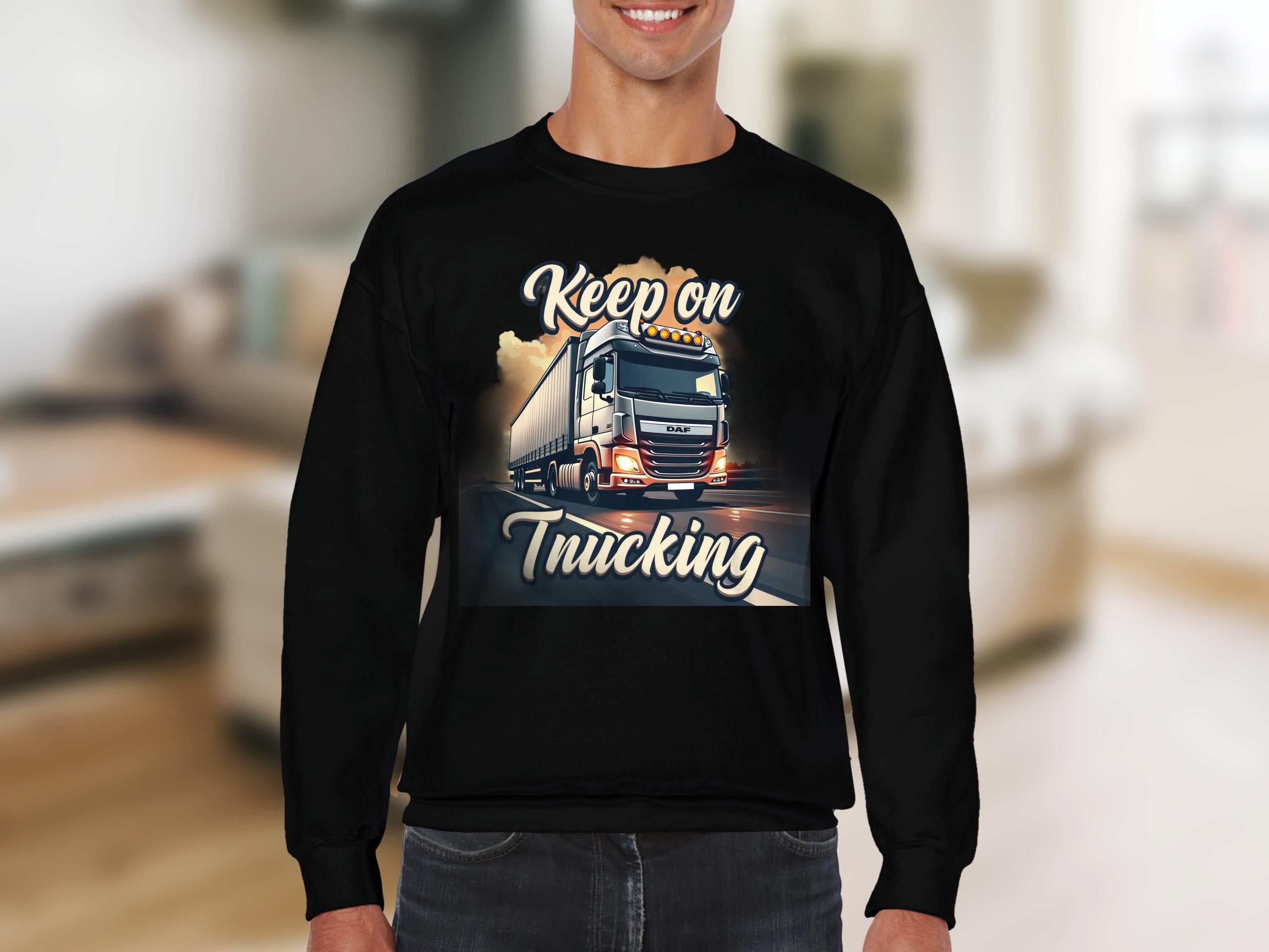 Dressed in Garment Graphics inspirational sweatshirt, the individual wears a black top with Keep on Trucking and a bold truck illustration, set against a beige couch and light floor, embodying open-road spirit.