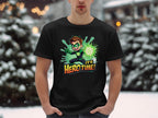 A person stands in the snow wearing a vibrant black Garment Graphics T-shirt featuring a cartoon character with a glowing green orb and the text Its Hero Time! Snow-covered trees and blurred lights provide the perfect backdrop for this superhero graphic print tee.