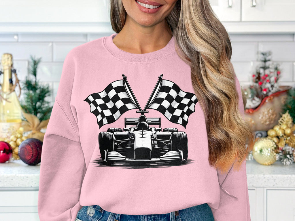 A woman in a festive kitchen wears a Garment Graphics sweatshirt featuring a race car and crossed checkered flags. Her long blonde hair is down, and she smiles amid the decorations.
