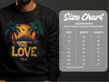 A person wears a black Garment Graphics One Love Sweatshirt, featuring a vibrant sunset between palm trees. The unisex design includes sizes from S to 5XL per the Gildan 18000 size chart, outlining width and length.