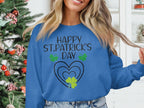 Someone is wearing a blue festive sweatshirt from Garment Graphics with Happy St. Patricks Day printed in black, highlighted by green clover designs and hearts, with a decorated Christmas tree as the backdrop.