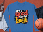 Garment Graphics presents their Graphic Art Sweatshirt: a blue, unisex sweatshirt featuring Its a Good Day to Laugh in bold colors. Perfect for any adventure, pair it with a water bottle, white towel, black shorts, and a basketball on any textured surface.
