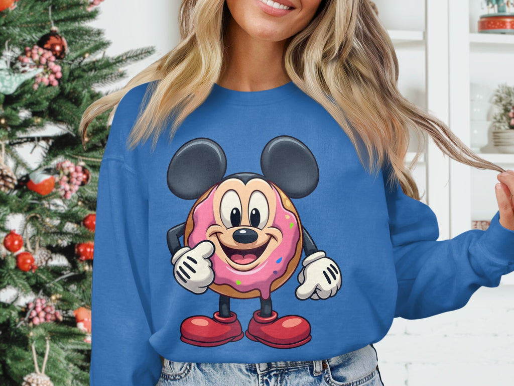 Someone in a Garment Graphics blue sweatshirt with a quirky donut design stands by a decorated Christmas tree and shelves with white decor. Their long, light hair enhances the festive vibe, showcasing the universal appeal of unisex-sized sweatshirts for all.