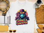 A Garment Graphics white sweatshirt captures Urban Style with a vivid graphic of a gorilla in sunglasses, hat, and chain necklace labeled Gorilla Gangster, showcased on wood with a scarf, notebook, pen, yellow purse, and coffee cup for added chicness.
