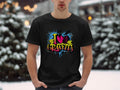 Wearing Garment Graphics black T-shirt with an I Love Graffiti design, a person stands outside against a snowy backdrop of blurred trees and lights, creating a serene contrast to the street art style. Their hands in dark pants pockets add to the laid-back look.