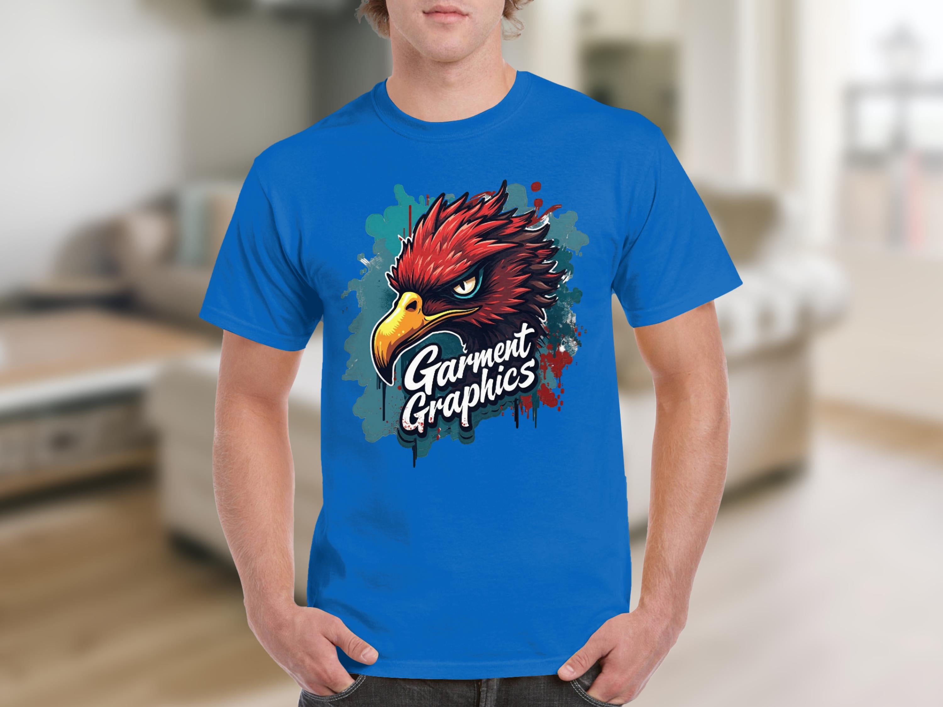 A person wears a classic fit blue T-shirt from Garment Graphics, featuring a vibrant eagle graphic, with an elegantly furnished interior softly blurred in the background.