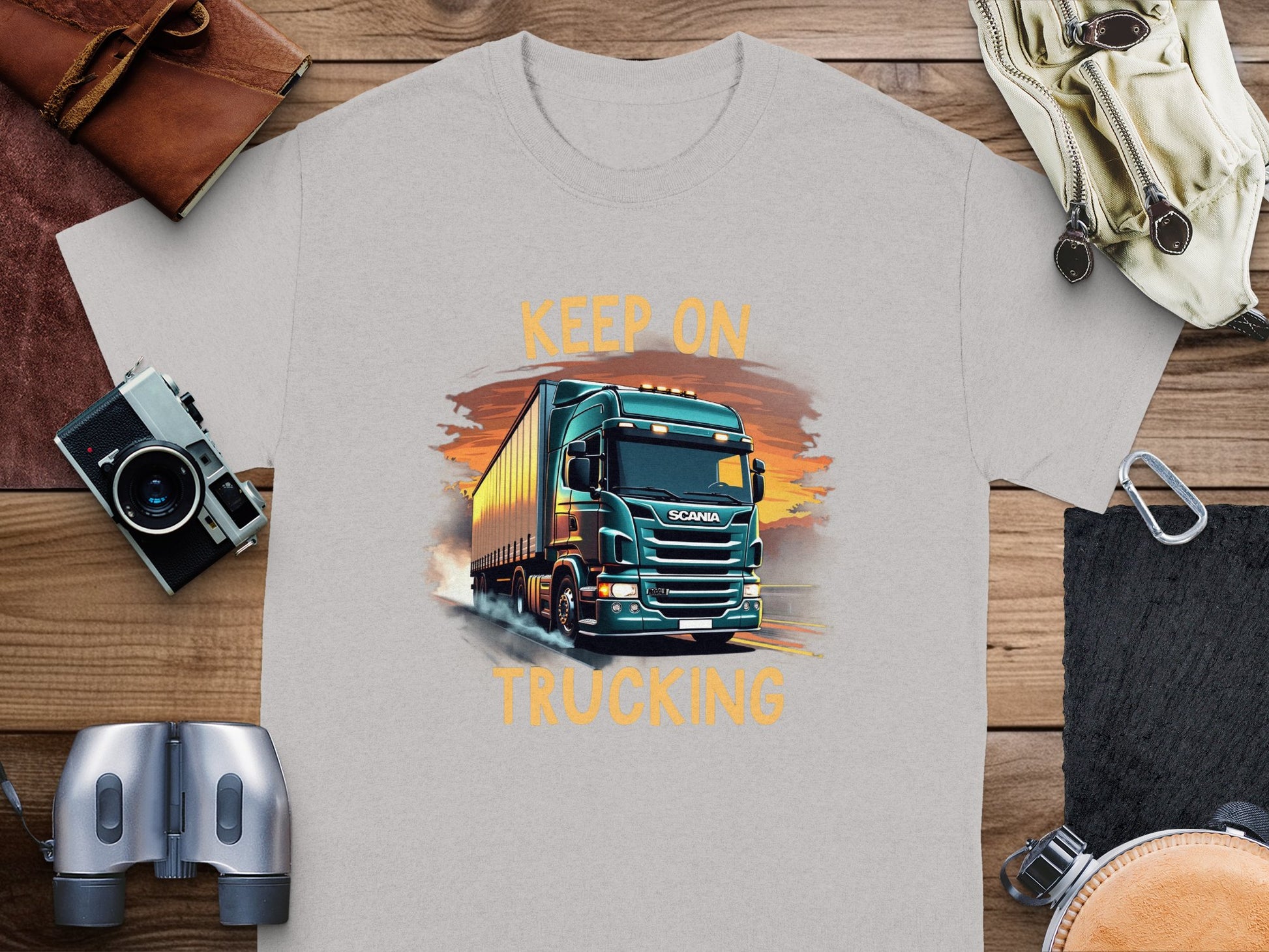 Garment Graphics offers a gray T-shirt for truck lovers with a vivid green semi-truck illustration against a sunset. Keep on Trucking is printed above and below, making it an ideal travel essential.