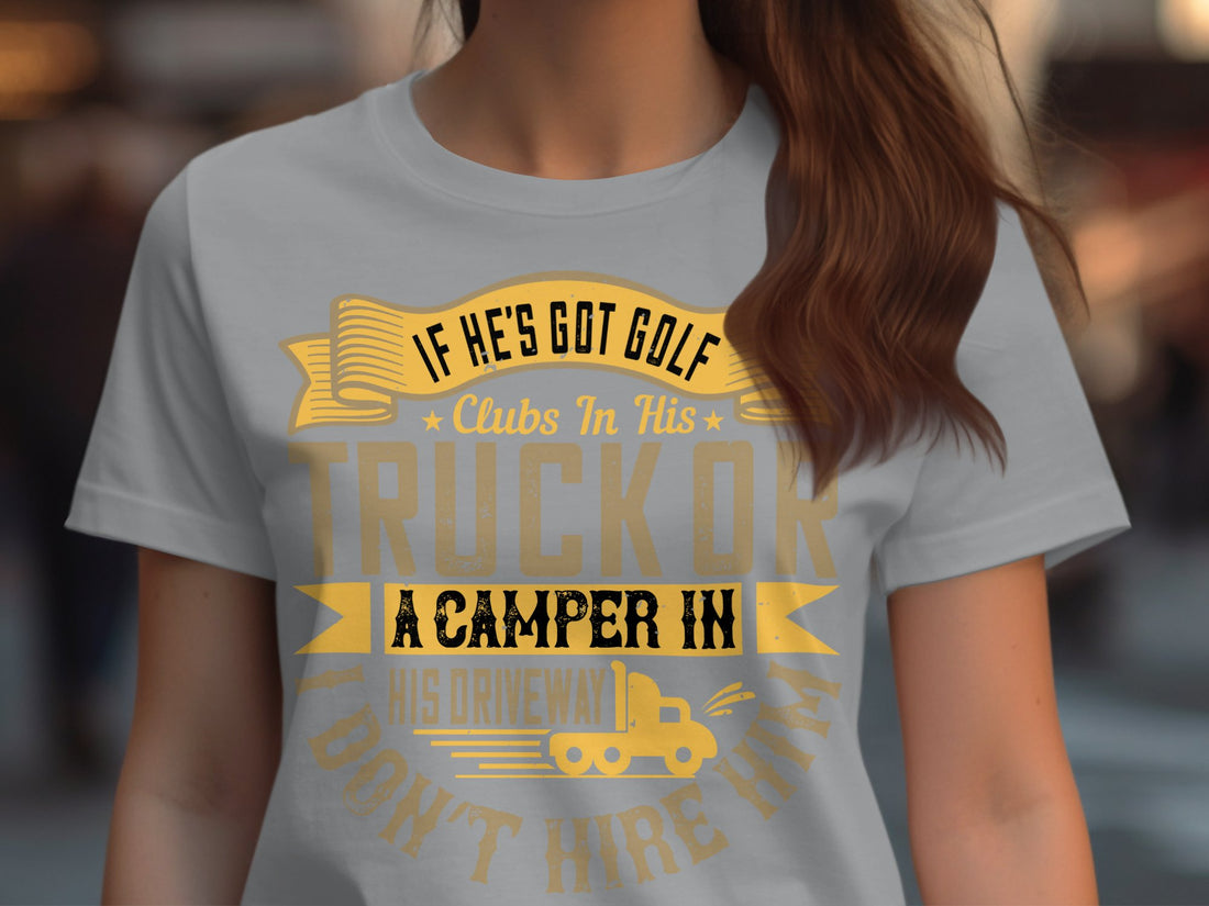 A womens white tee from Garment Graphics displays a humorous golf graphic with the text, If hes got golf clubs in his truck or a camper in his driveway I dont hire him, set against wrapped gifts, a knitted sweater, candy cane, and festive decorations on a wooden backdrop.