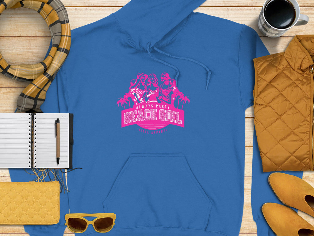 A vibrant blue Garment Graphics hoodie with Always Party Beach Girl in pink is stylishly displayed on wood, paired with yellow shoes, a matching purse, chic sunglasses, a patterned scarf, a notebook and pen, and a coffee cup for the perfect laid-back vibe.