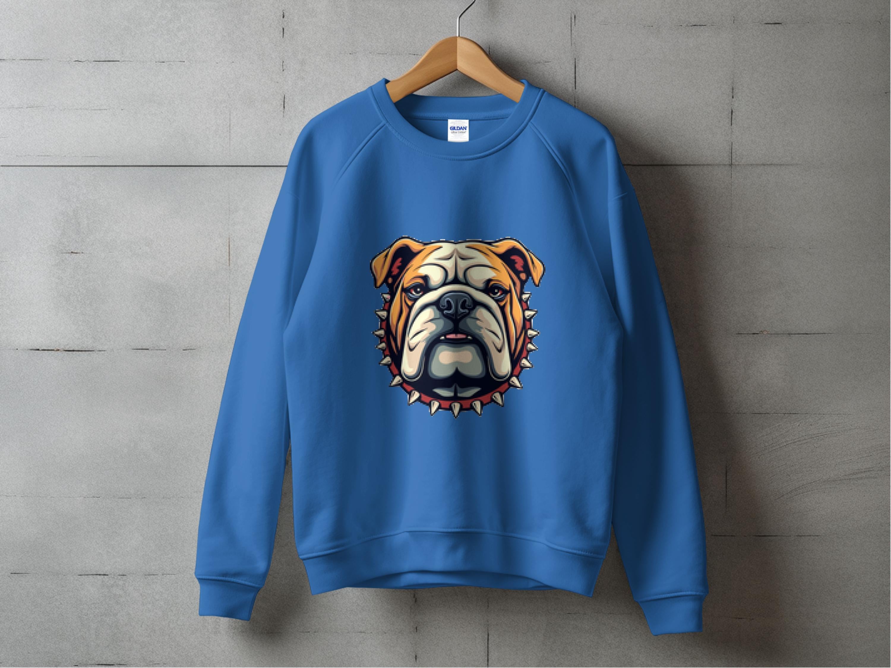 Displayed on a wooden hanger against a concrete wall, Garment Graphics blue sweatshirt features a bulldog graphic with a spiked collar. Available in unisex sizes, this piece effortlessly combines comfort and style.