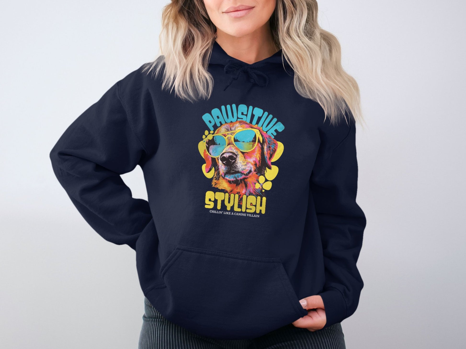 A person dons a vibrant navy hoodie by Garment Graphics, showcasing a colorful dog with sunglasses and PAWSITIVE STYLISH text. It perfectly complements their unique style as they stand against a plain background, hands in pockets.