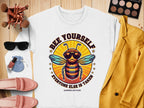 A flat lay features Garment Graphics white Summer Edition sweatshirt adorned with a bee in sunglasses and BEE YOURSELF EVERYONE ELSE IS TAKEN. It’s paired with trendy sunglasses, makeup essentials, a yellow jacket, pink shoes, and brushes—all highlighting unisex sizing.