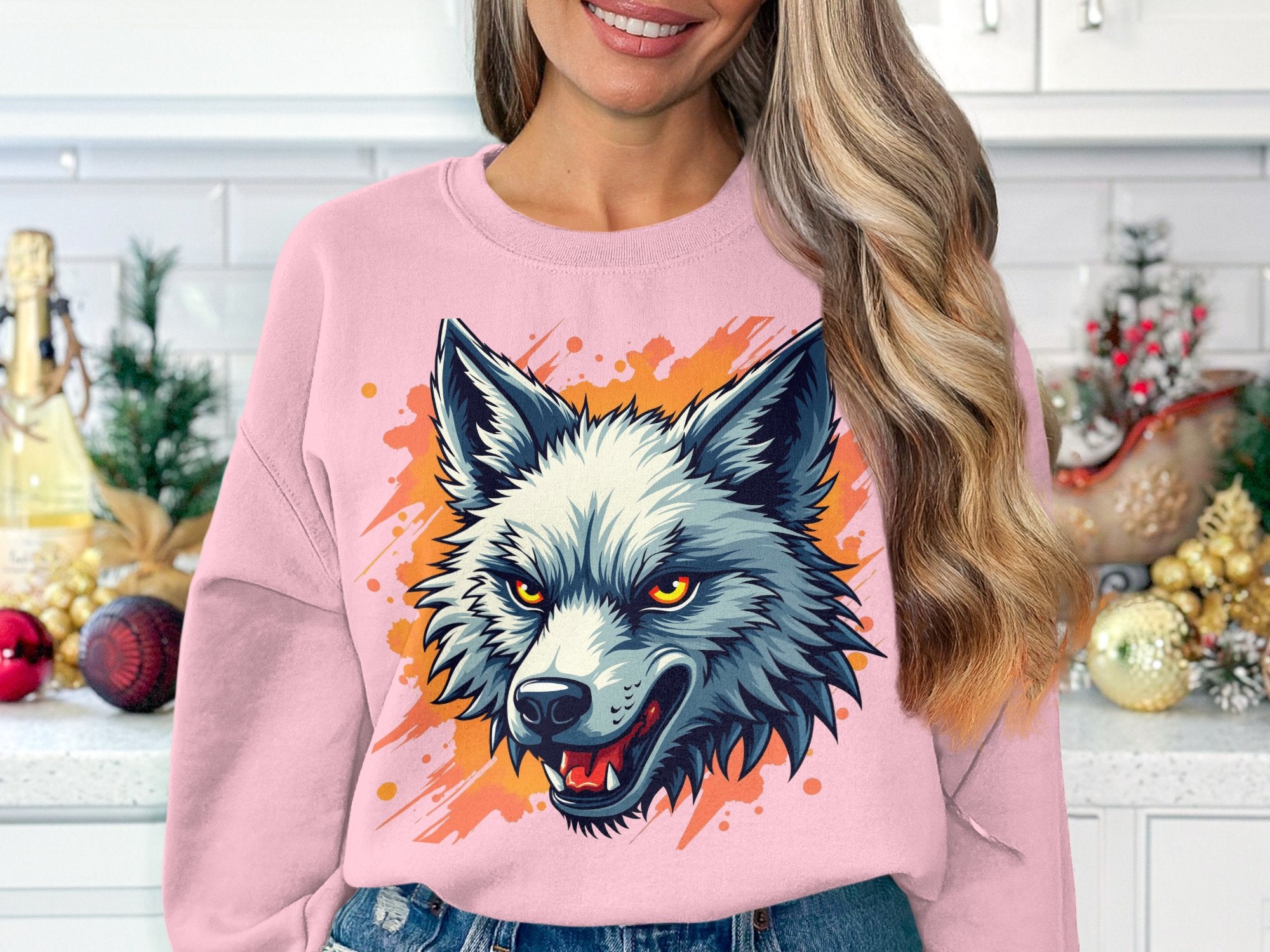 In the kitchen, a woman sports a bold Garment Graphics sweatshirt with a fierce wolf design on an orange-splattered background, while festive ornaments and a reindeer add holiday flair behind her.