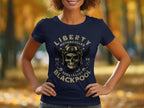 A person sports a Garment Graphics navy T-shirt featuring a skull and wings, paired with goggles and a helmet. The shirt reads, Liberty Motorcycles Specialist Blackpool 2023, set against an outdoor background of blurred autumn leaves.