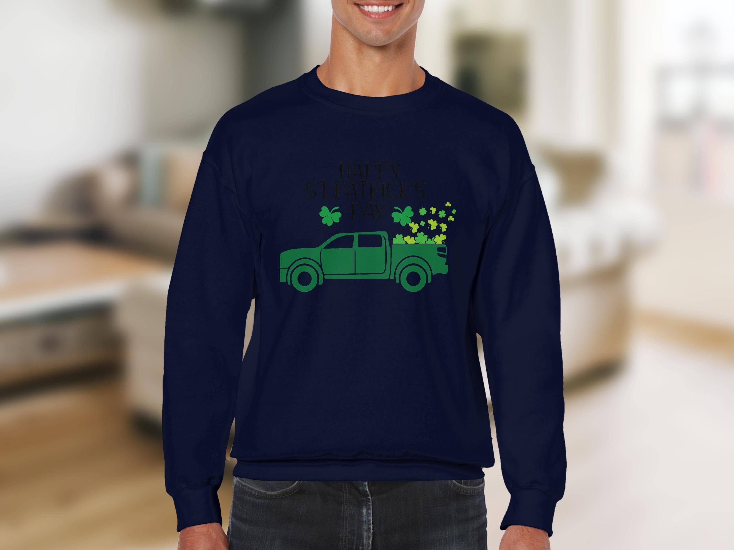 A person dons a Garment Graphics navy sweatshirt with a green pickup truck design packed with shamrocks, celebrating Happy St. Patricks Day. The indoor background is softly blurred.