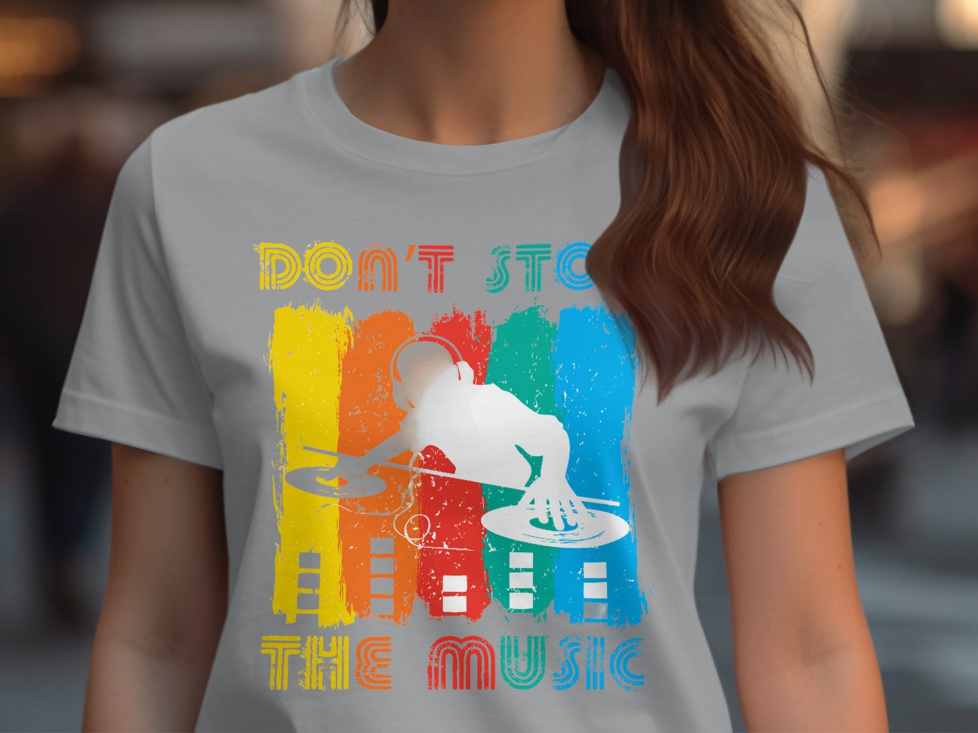 A music enthusiast sports a light gray DJ graphic tee from Garment Graphics, featuring dynamic vertical paint streaks in red, yellow, blue, and green with a central white silhouette of a DJ at turntables. The text reads Dont Stop the Music.