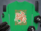 The Garment Graphics Howdy Rodeo sweatshirt, ideal for rodeo enthusiasts, showcases a striking cowboy on horseback with Not for Rookies, surrounded by a smartphone, speaker, smartwatch, sneakers, and dumbbells, embodying the cowboy spirit with style.