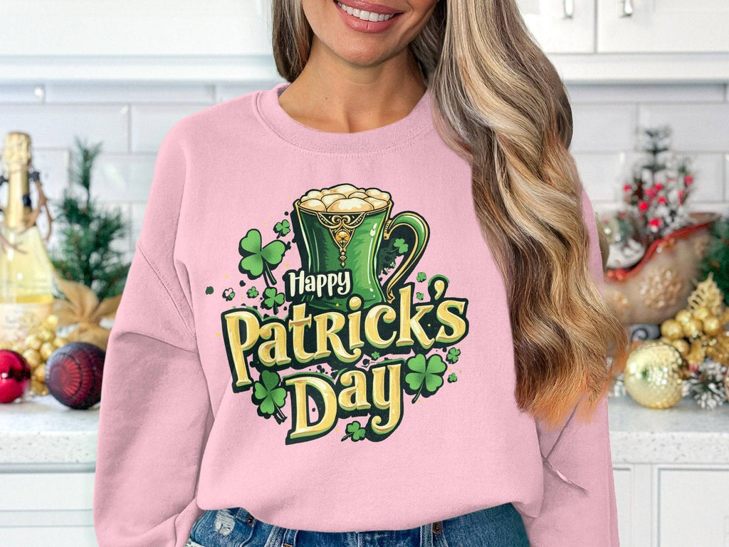 In a kitchen, a woman wears a vibrant light pink sweatshirt by Garment Graphics featuring a St. Patricks Day design with a green mug adorned with shamrocks and the text Happy Patricks Day. Decorative items enhance the background charm.