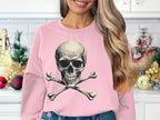 A woman showcases an edgy style in a Garment Graphics pink sweatshirt with a skull and crossbones design. Her long, wavy hair enhances the looks flair. Kitchen cabinets and festive decorations create a vibrant backdrop.